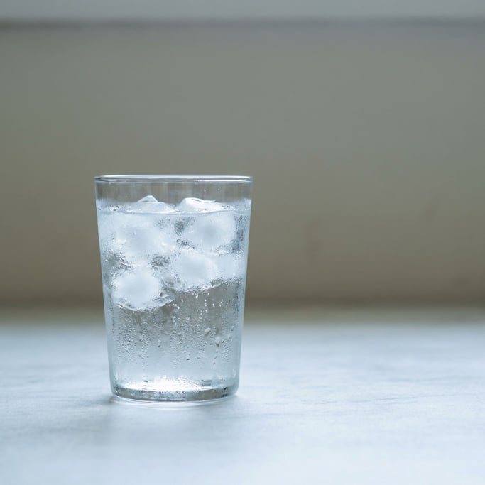 A clear glass of sparkling water with ice, condensation on the glass, cool light (w8rrv2l)