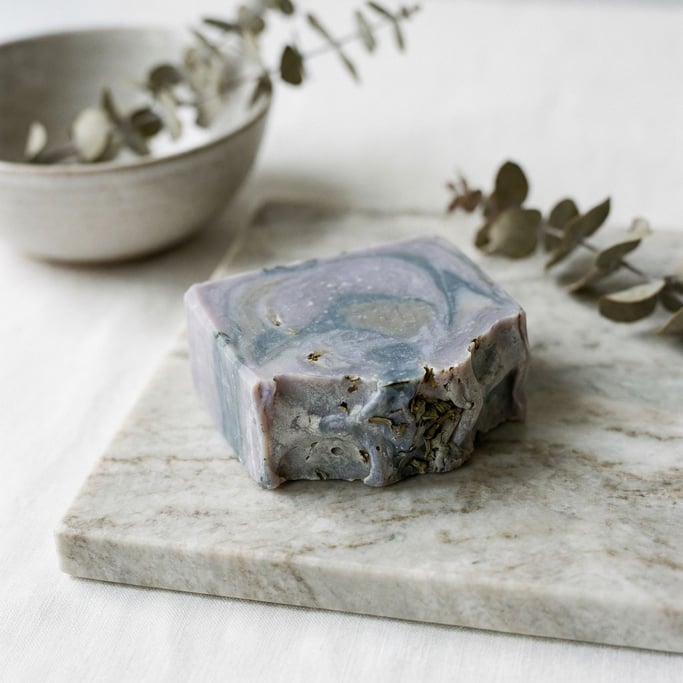 A bar of handmade soap in cool lavender tones, resting on a marble slab (i6xlivs8)