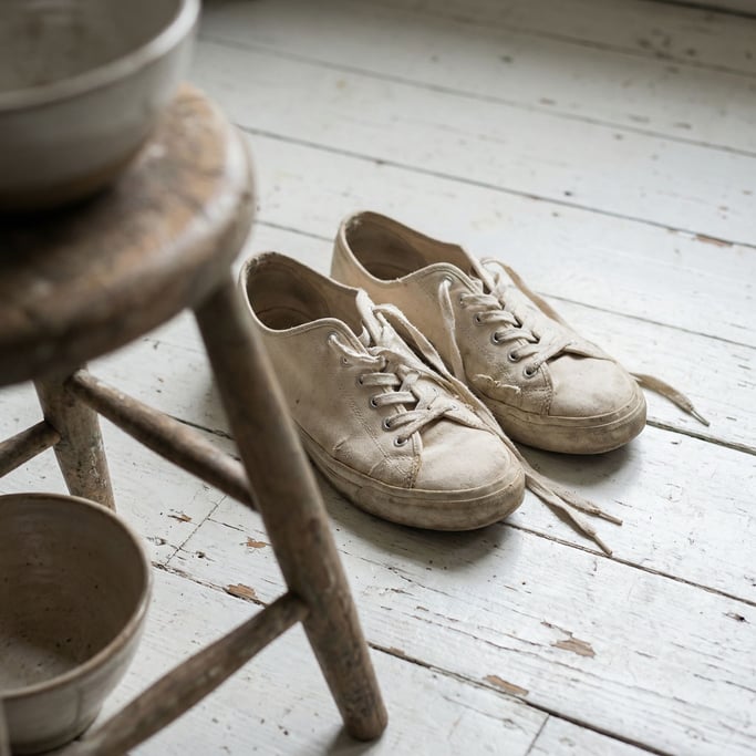 A pair of raw canvas sneakers on a whitewashed wood floor, laces untied, casual and lived-in (ergby2ny)