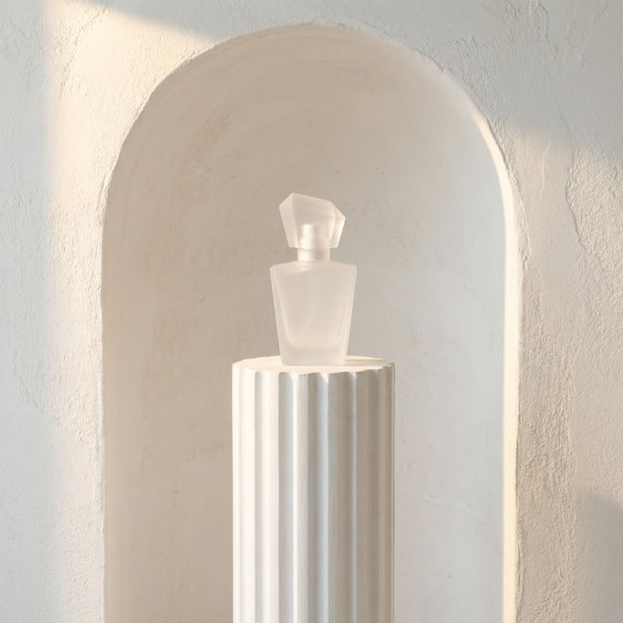 A single perfume bottle with an angular geometric cap in frosted white glass on a tall slender plast