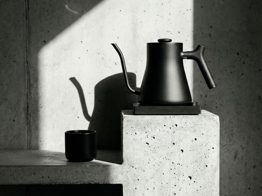 A matte black electric kettle with a gooseneck spout on a rough concrete countertop-style pedestal