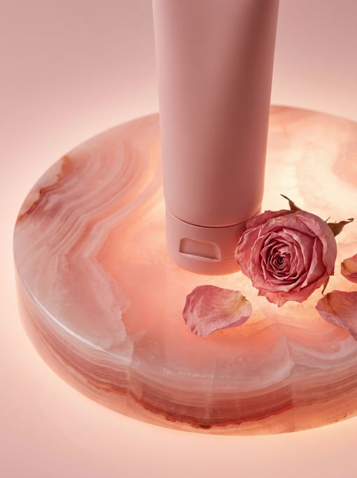 A tube of hand cream in matte blush pink on a circular pink onyx stone pedestal