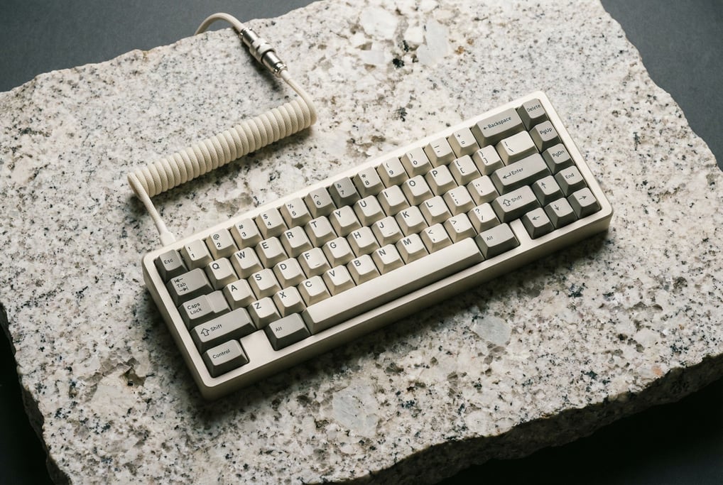 A mechanical keyboard in cream and grey keycaps on a large piece of raw light-colored granite