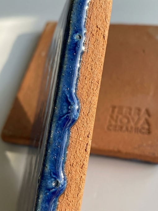 The boundary where glossy deep blue glaze meets raw terracotta bisque on a ceramic tile edge — abrupt and beautiful