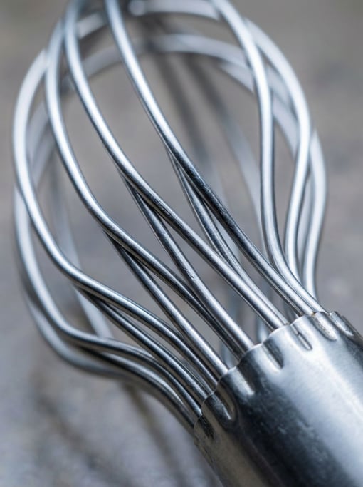 Macro photograph of a whisk's wire loops showing the precise bending where each wire meets the handle ferrule