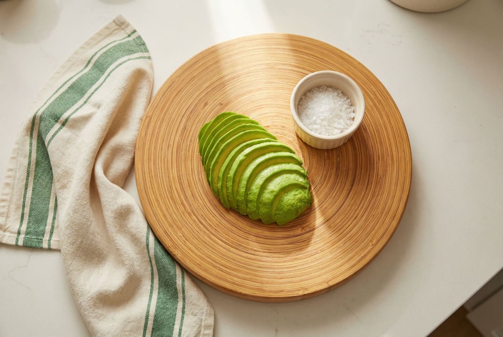 A bamboo cutting board holding sliced avocado and a small ceramic ramekin of sea salt