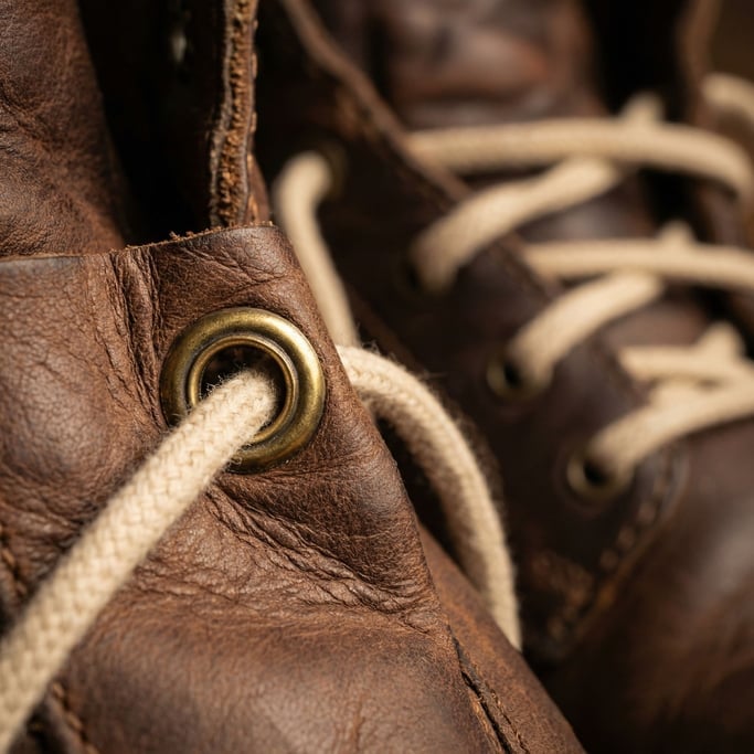 Extreme close-up of a shoe eyelet showing the brass grommet punched through the leather upper