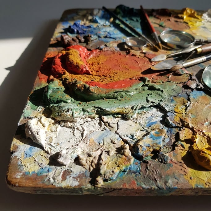 An archaeological dig in pigment: thick accumulated layers of dried oil paint on a palette reveal a miniature landscape of color peaks and valleys