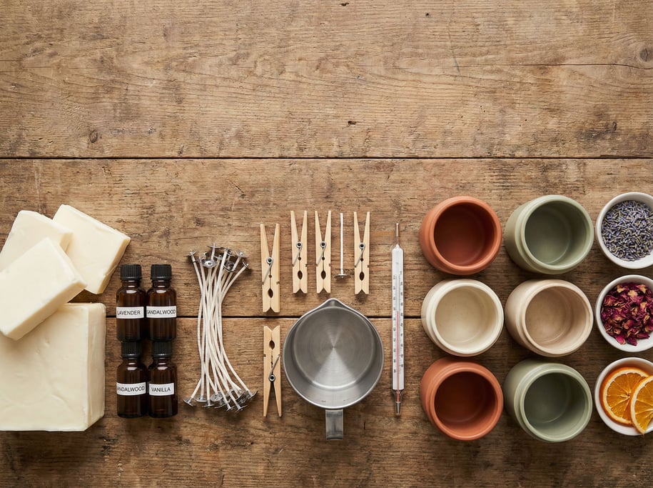 Flat-lay arrangement of a candle maker's supplies on a raw wooden work surface