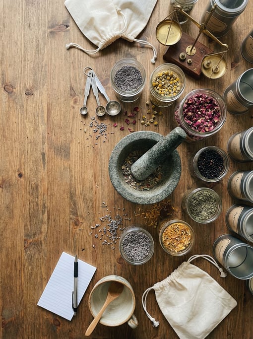 Flat-lay of a herbalist's tea blending station on a wooden counter