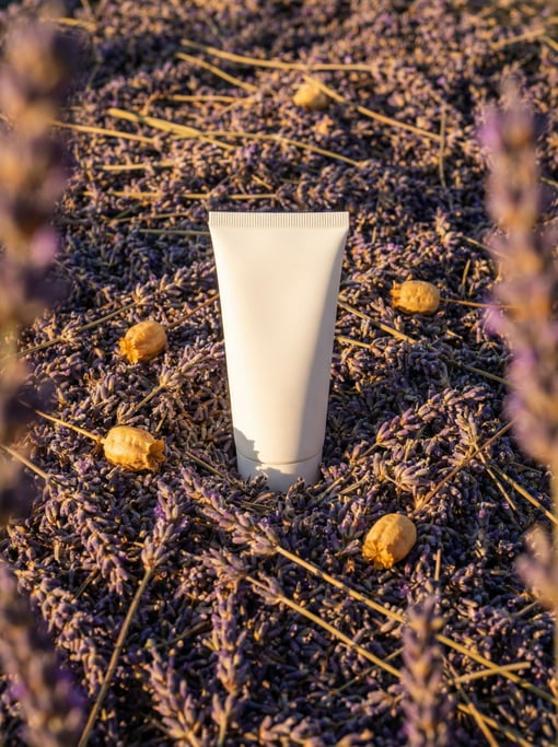 A tube of hand cream emerging from a bed of dried lavender stems in full bloom