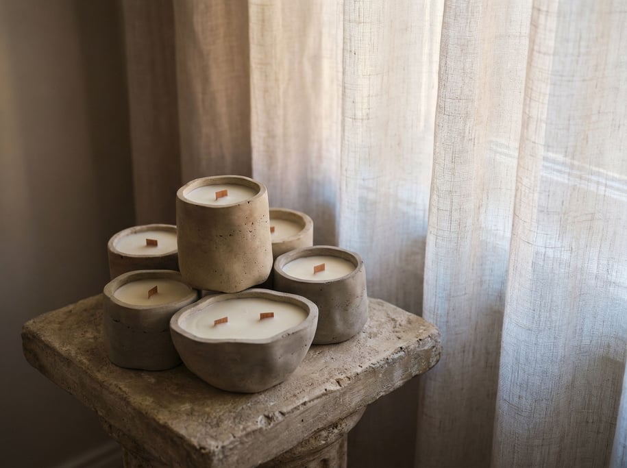 Hand-poured candles in raw concrete vessels, arranged asymmetrically on a stone surface (gex6aj)