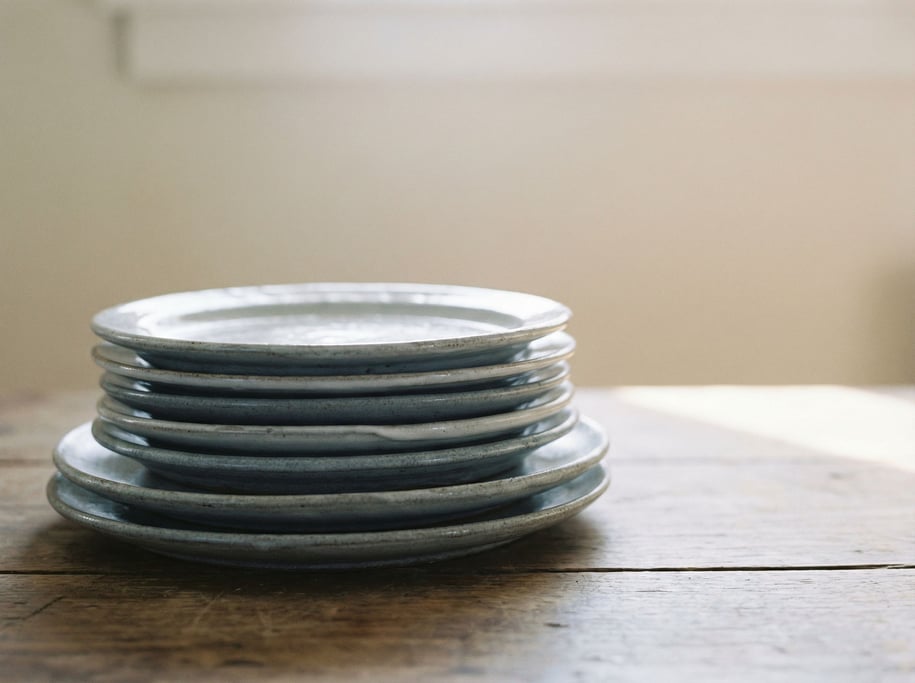 A stack of handmade ceramic plates in cool gray tones, slight imperfections visible, side lit (roklras)