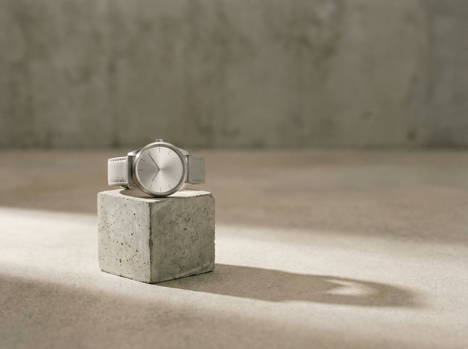 A minimalist watch on a concrete display block, brushed steel case, soft overhead light (rmftqxc)