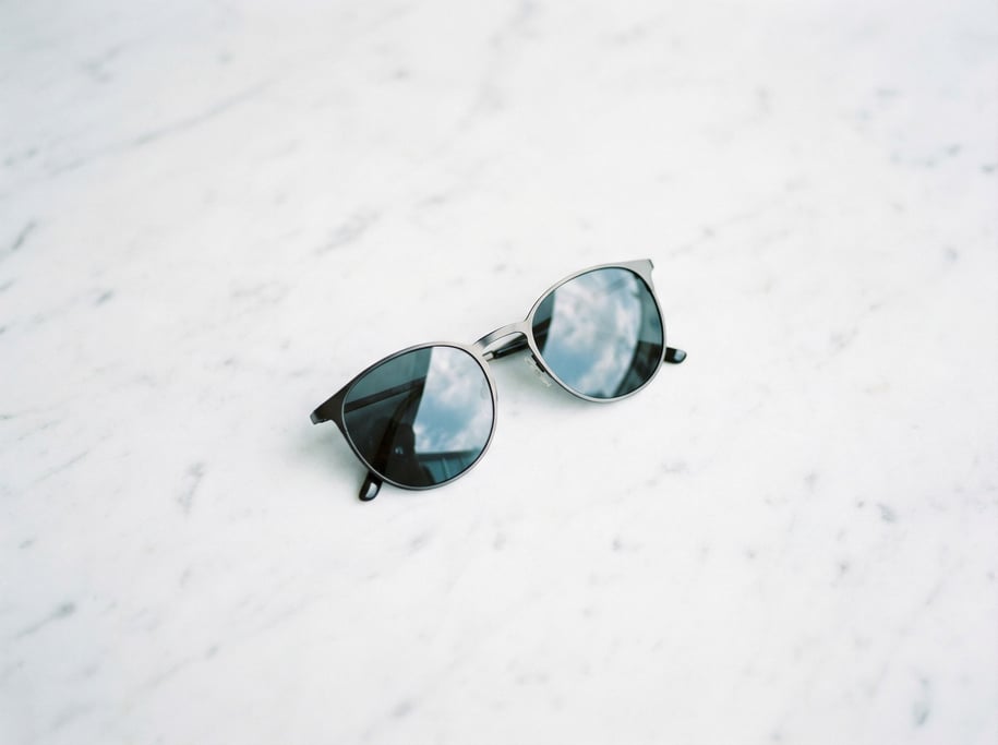 A pair of sunglasses on a white marble surface, reflections in the lenses, cool tones