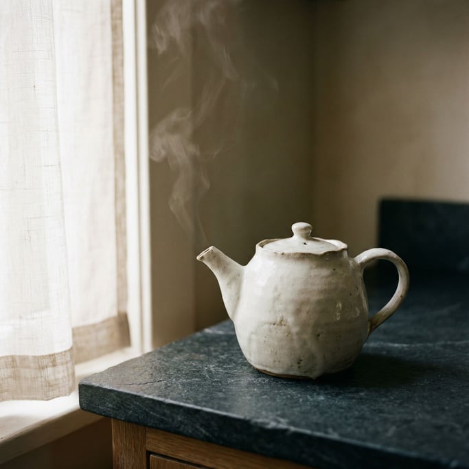 A white porcelain teapot on a dark stone counter, steam rising, minimal and clean (6muncgdx)