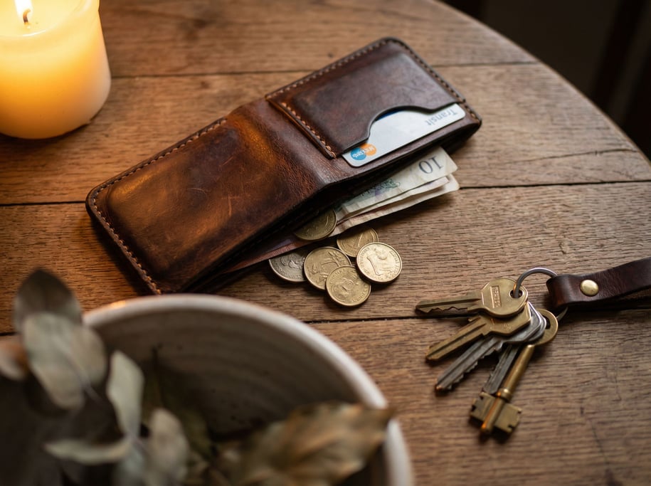A hand-stitched leather wallet, aged to a rich patina, contents spilling slightly, keys beside it (a2ggnzg3)