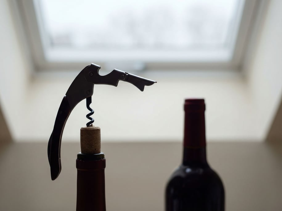 A corkscrew and wine cork mid-pull, red wine bottle in soft focus behind, ritual of opening (lnzg7ap3)