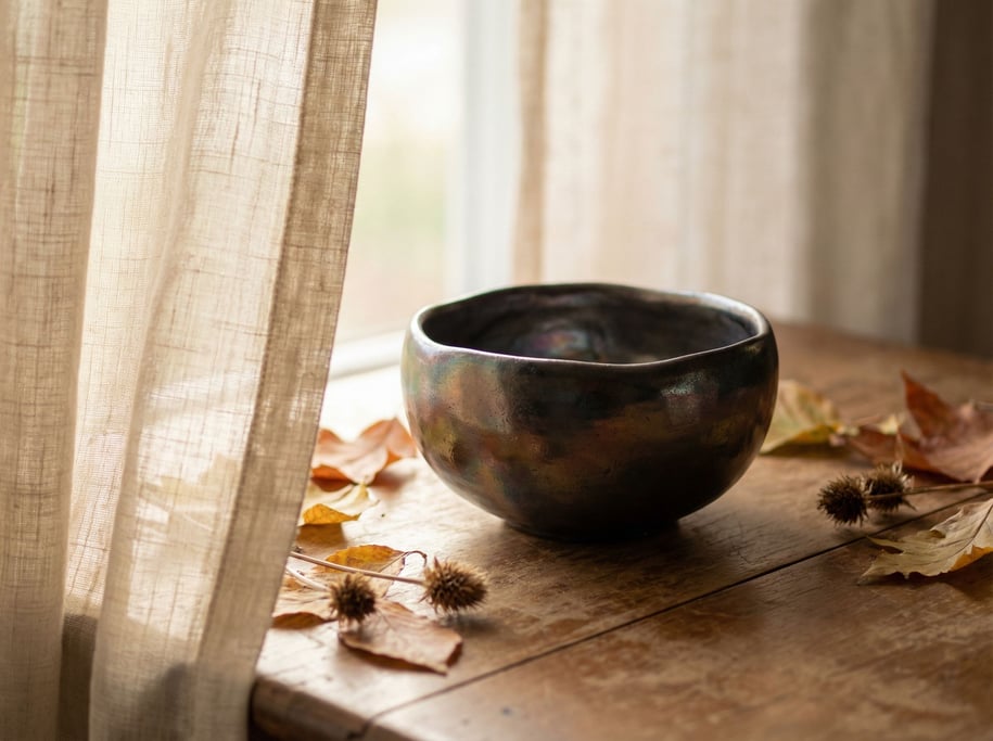 A hand-thrown raku tea bowl, irregular form, metallic glaze catching light at every angle (yyjvzsm)