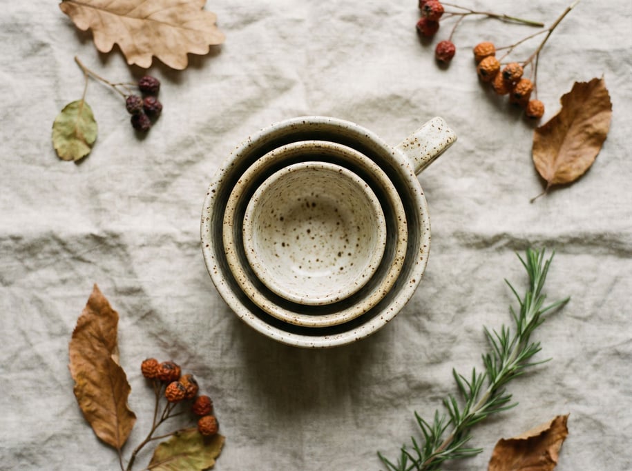 Three speckled ceramic cups in graduating sizes, nested together, overhead on a linen cloth (l6pnhqx2)
