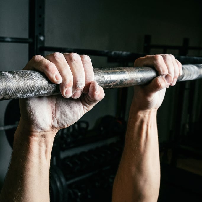 Close-up of chalk-covered hands gripping a textured steel pull-up bar, knuckles white with effort