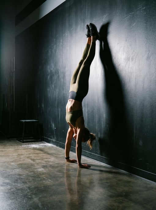Full-body shot of a fit woman doing a handstand against a dark gym wall, perfect form