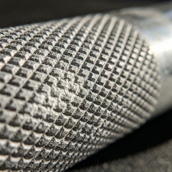 Extreme close-up of a barbell knurl pattern on a steel bar, chalk residue in the grooves