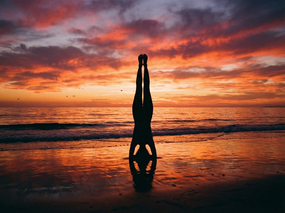Yoga practitioner in a perfect headstand on a beach at sunset