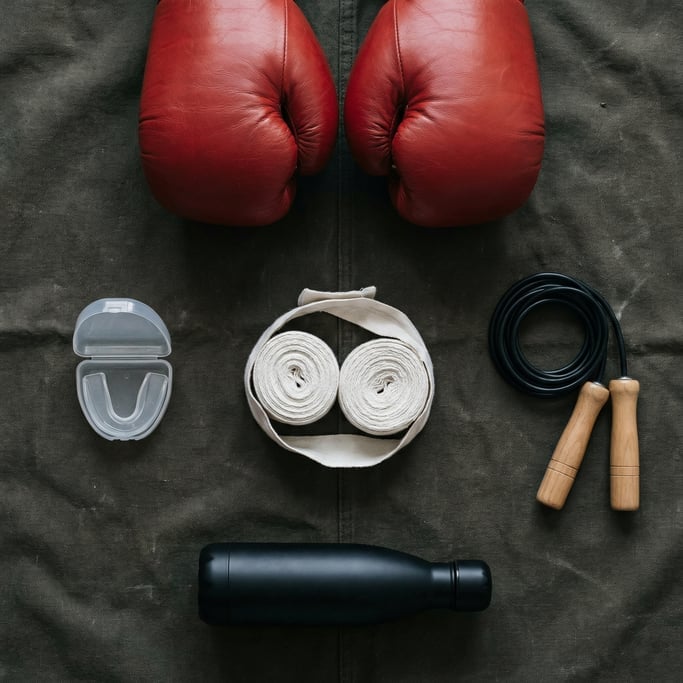 Flat lay of boxing gear on dark canvas: red leather gloves, white hand wraps, mouth guard