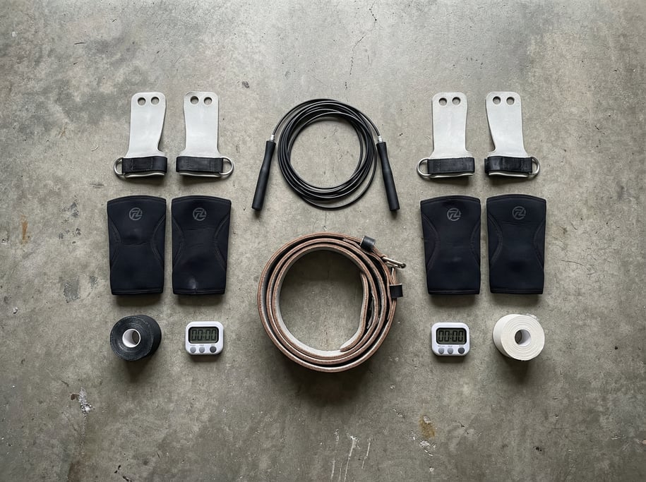 Flat lay of CrossFit equipment on grey concrete: jump rope, gymnastic grips, lifting belt