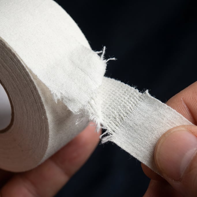Close-up of athletic tape being unrolled from a roll, the white cotton tape partially torn