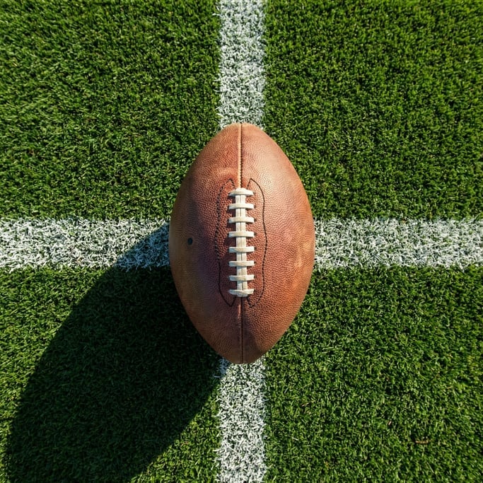 Overhead shot of a football on fresh-cut emerald green grass with white yard line markings