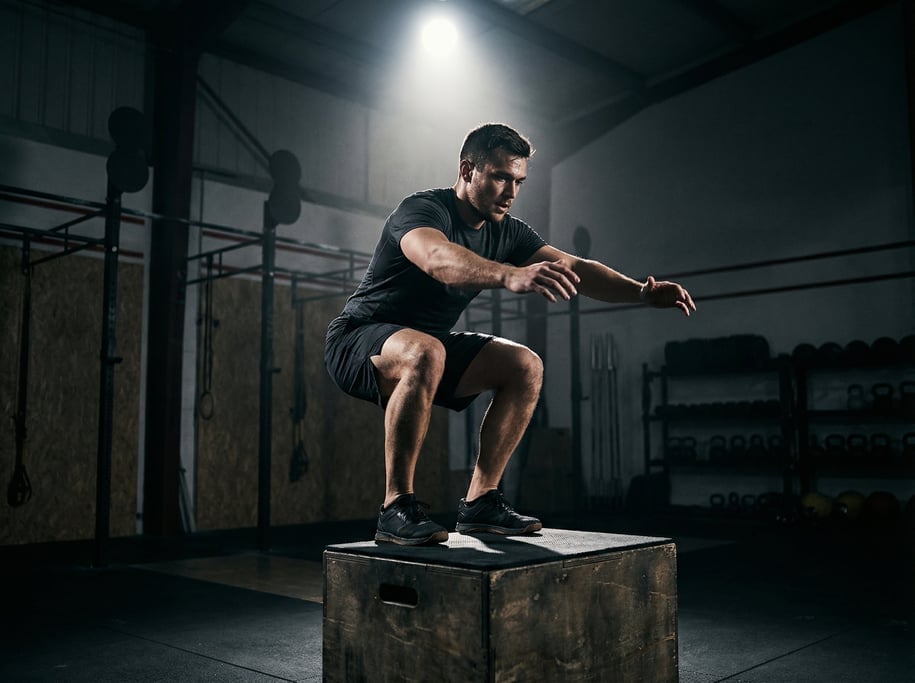 Athlete performing box jumps onto a tall plyo box, caught at the landing position on top