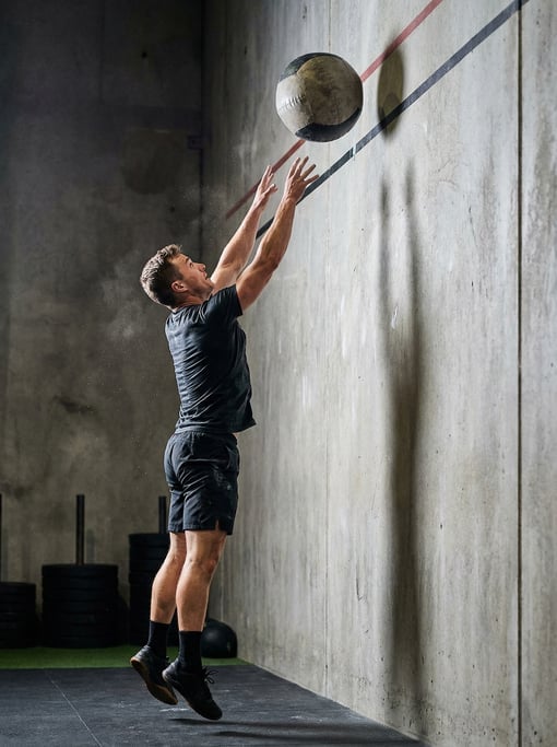 Wall ball exercise at full extension: athlete releasing a heavy ball toward a target line on a concr