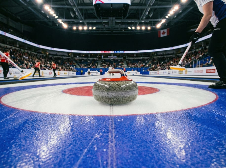 Curling stone gliding across the ice toward the house target rings