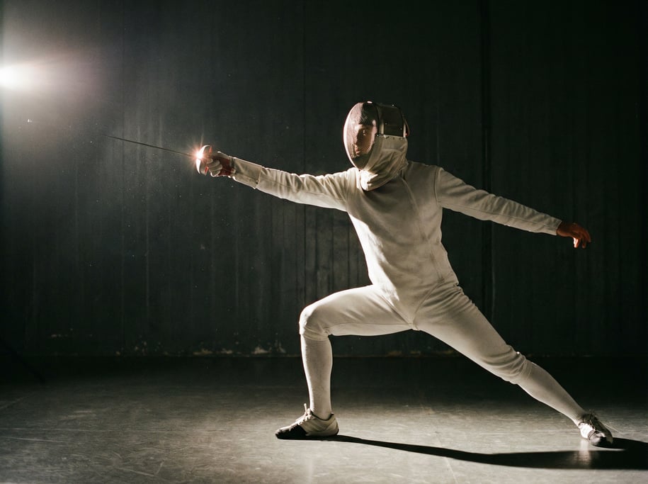 Fencer in full lunge position, foil extended, white uniform against dark background