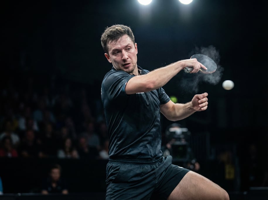 Table tennis player mid-backhand smash, the ball a blur, intense focus and body rotation