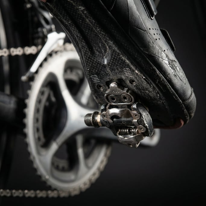 Close-up of a cycling shoe clipped into a pedal, the carbon sole and cleat mechanism visible