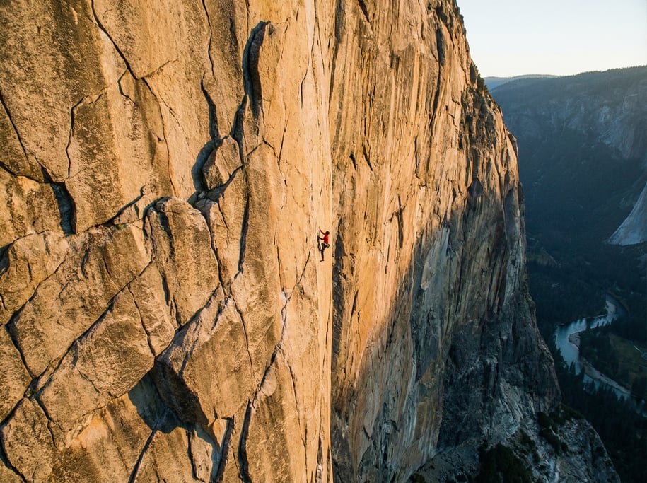 Free solo climber on a massive granite wall, tiny figure against vast stone