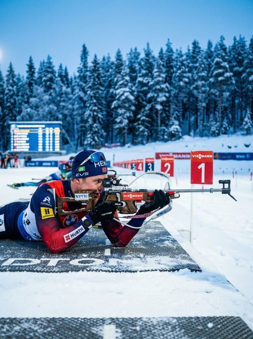 Biathlon competitor prone on the shooting mat, rifle aimed at distant targets, snow-covered range