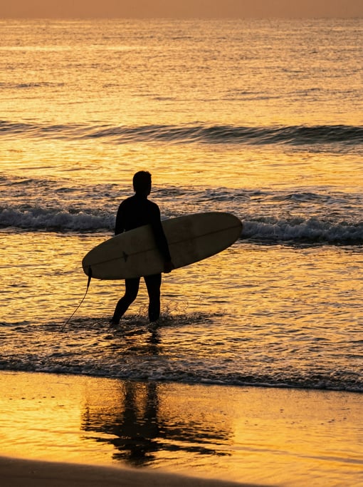 Surfer walking into the ocean at sunrise holding a longboard under one arm