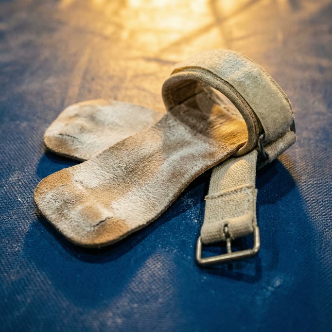 Close-up of a gymnastics hand grip with leather palm pad and wrist strap, chalk-covered