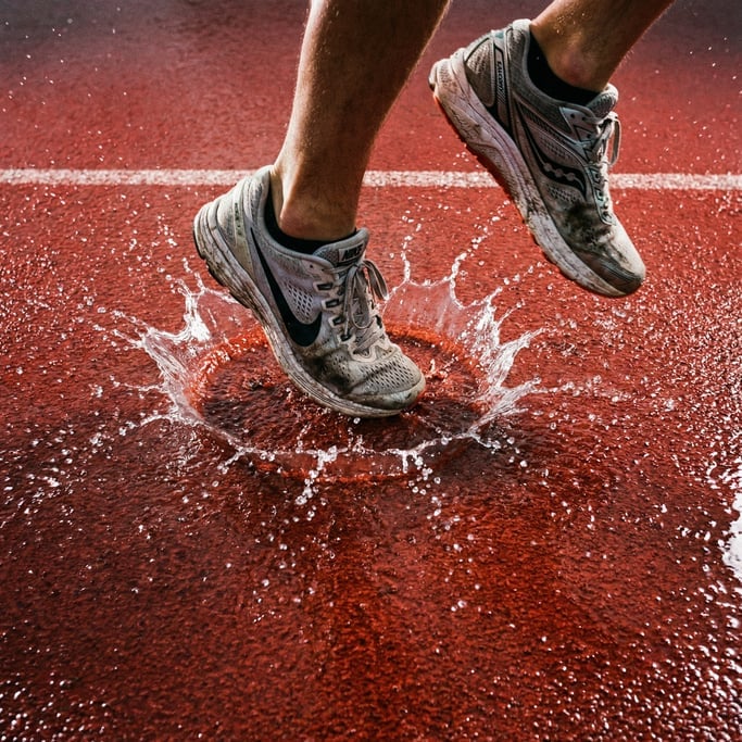 Overhead shot of athletic shoes mid-stride on a wet track surface, the splash pattern frozen