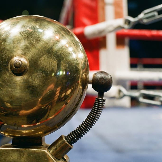 Close-up of a boxing ring bell, the polished brass surface catching arena light
