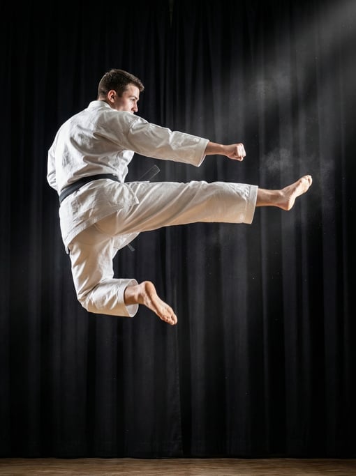 Martial artist performing a flying side kick, both feet off the ground, white gi flowing