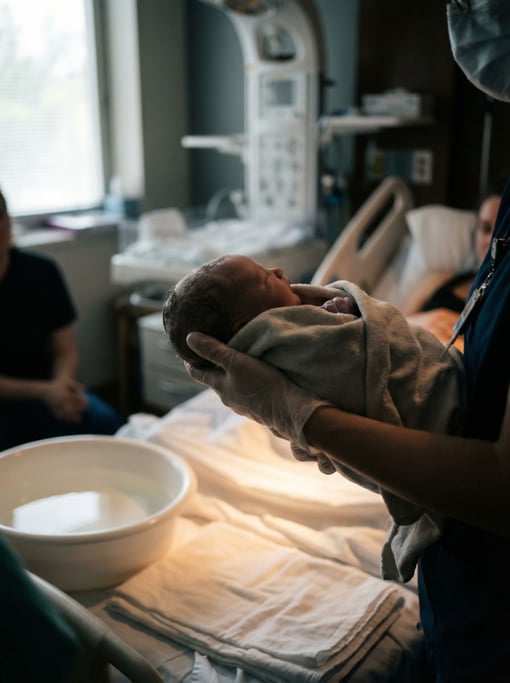 A midwife's calm hands guiding a newborn, intimate hospital room, soft overhead light