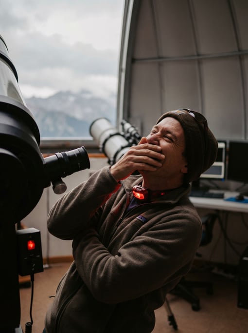 An astronomer at a telescope in a mountaintop observatory, red light preserving night vision (cjetouh4)