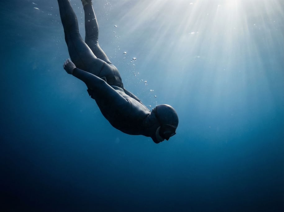 A free diver descending into blue water, body streamlined, light rays from the surface above (sf3vfp4j)