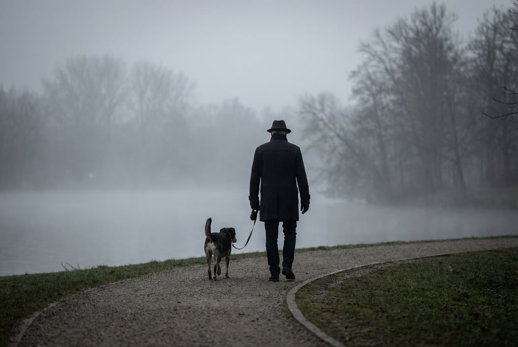 A man in his 50s walking his dog along a misty lakeside path