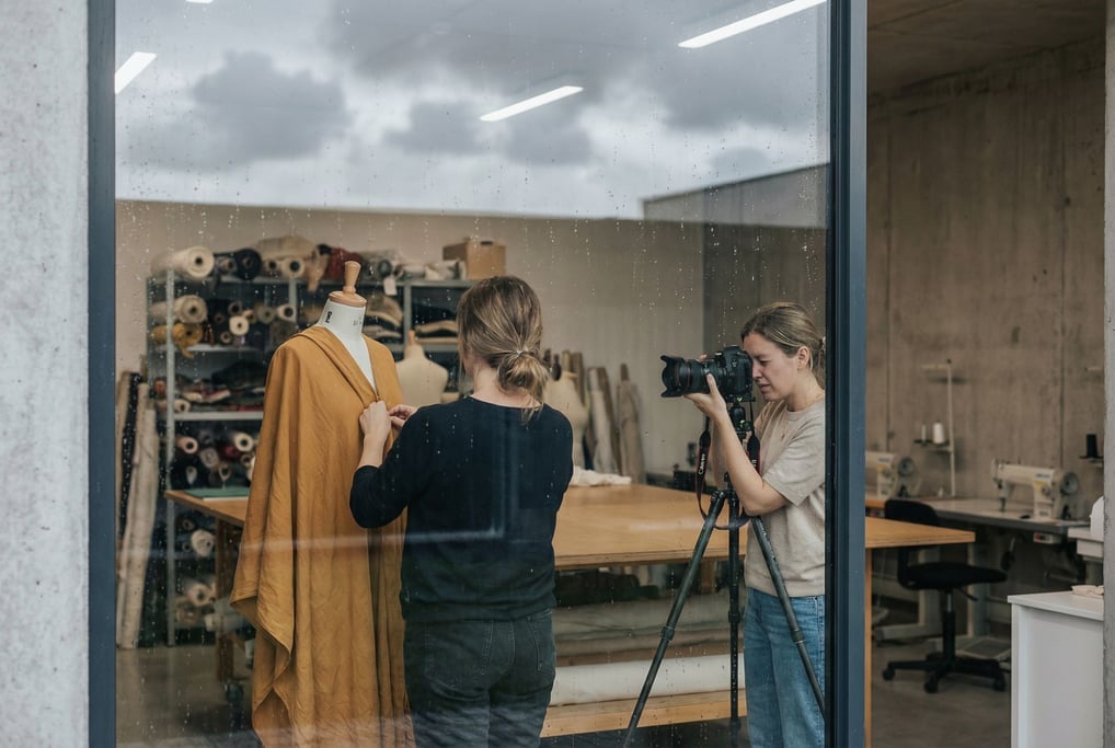 Two women in a glass-walled studio taking reference photos of fabric draping